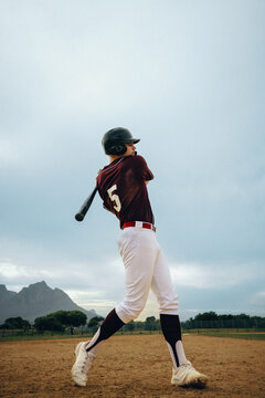 Baseball player in uniform practicing swing during training with scenic mountain background
