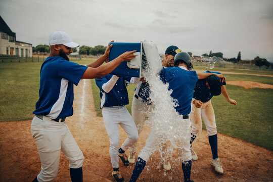 Baseball team celebrates victory with water cooler splash on field - Powered by Adobe