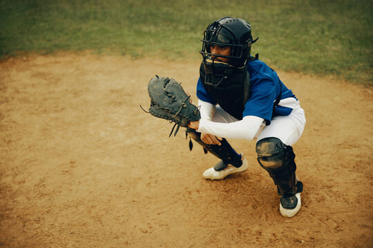 Baseball catcher in full gear crouching on the field, holding a mitt and wearing shin guards and helmet during a game