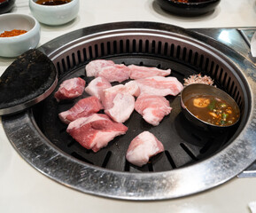 Grilling pork meat on a iron BBQ board in Korean restaurant.