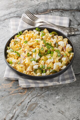 Mexican Street Corn Potato Salad with spicy jalapenos, boiled eggs, fresh green and red onions, and salty cotija cheese closeup on the plate on the table. Vertical