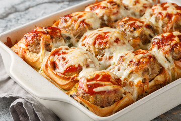 Homemade baked sliders stuffed with meatballs, topped with tomato sauce and grated cheese close-up in a baking dish on a table. horizontal