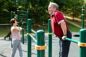 Fototapeta premium Elderly man doing exercises on a horizontal bar at an outdoor sports ground