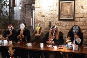 People play mafia wearing masks at a table in a cafe.