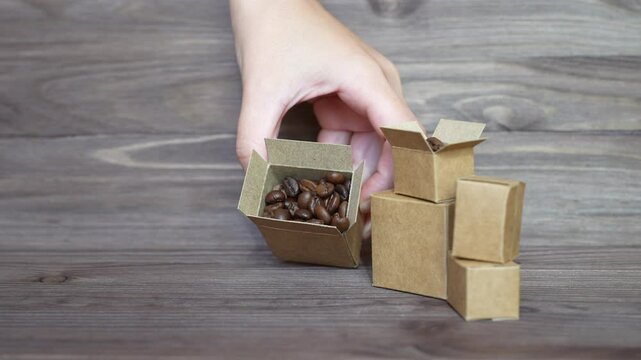 Hand takes small open boxes while coffee beans and empties them on a wooden table, showcasing packaging and coffee products.