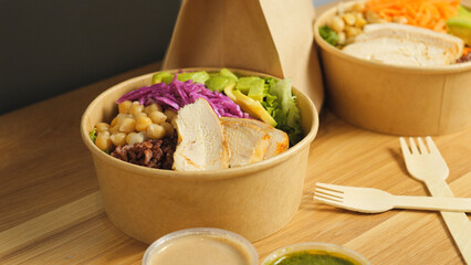 Nutritious buddha bowls featuring grilled chicken, chickpeas, red cabbage, avocado, brown rice, and lettuce on wooden background, representing balanced eating