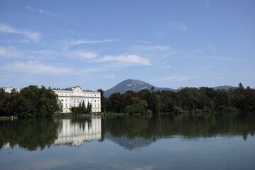 Obraz premium Serene view of Salzburg's landscape featuring a historic building and reflecting lake under a blue sky
