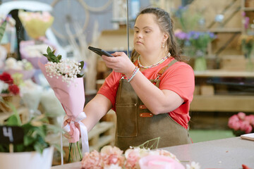 Medium close up of young Caucasian florist holding small bouquet with gypsphila while taking high angle hot of it to post on social media
