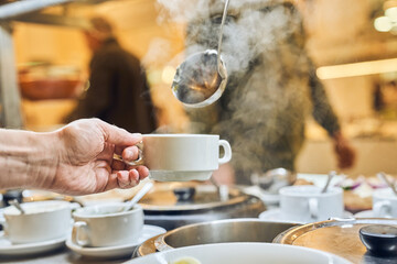 Close-up of a hand against a background of steam pouring hot soup with a ladle. Free food in the charity canteen, with space for copying. High quality photo