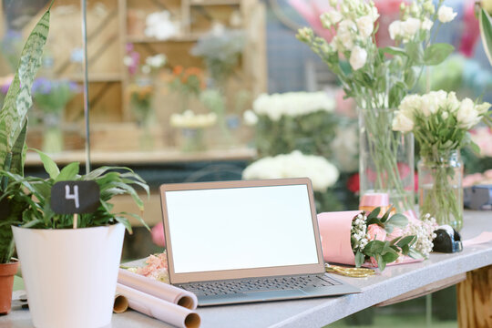 Medium close up of table with laptop, small tender bouquet and wrapping paper rolls