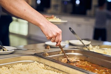 The hand of an unrecognizable volunteer puts nutritious food on a plate in a modern charity canteen. High quality photo