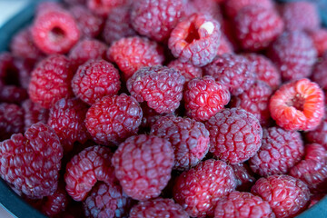 A bowl of red raspberries. The raspberries are ripe and ready to eat. The bowl is black and the...
