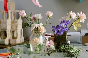 Medium close up of pastel pink roses and purple orchid in crustal vase on table covered with fresh and green ruscus