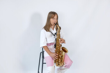 Naklejka premium Girl playing, practicing the saxophone, playing a melody on a musical instrument, sitting on black chair on white background. Out-of-school children activities, lessons