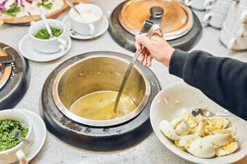 A woman's hand holds a ladle in a saucepan. Meat broth soup with fresh vegetables. Buffet in the restaurant complex with copy space. High quality photo
