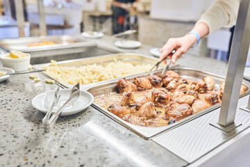 Delicious dishes for a late dinner in metal containers. There are tongs in his hand for laying chicken. A useful buffet in the restaurant at the event. High quality photo
