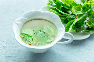 Mint tea. A cup of peppermint tea with fresh mint leaves, on a blue background