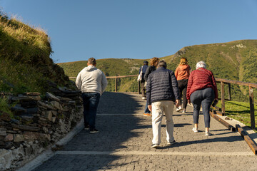 A group of people are walking up a hill. The hill is covered in grass and rocks. The people are walking on a stone path. The sky is blue and clear