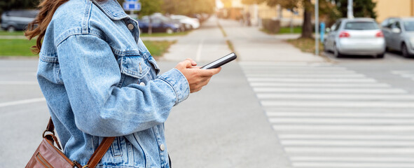 Mobile phone in the hands of a woman wearing casual clothes on a city street