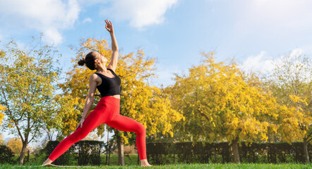Fit and healthy woman wearing sportswear practicing yoga outdoors on a green lawn in a city park. 