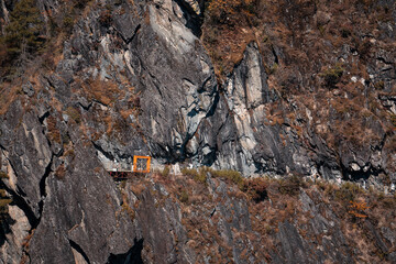 A narrow path clings to a steep, rocky mountainside in Yunnan, China, near Dali.  The landscape is rugged and brown, with a small orange structure visible on the path.