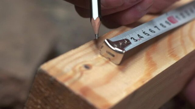 Close-up of hands marking precise measurements on a wooden plank using a pencil and a measuring tape