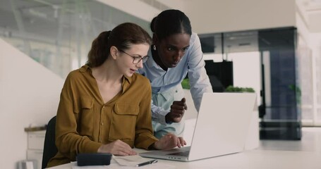 Two women colleagues collaborating, engaging in discussion, working together on joint tasks involving calculations, data analysis or financial planning met in contemporary office. Teamwork, accounting