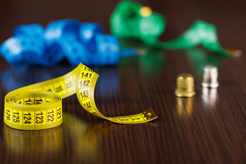 Tailor's measuring tapes of different colors and thimbles for sewing lie on a dark wooden table....