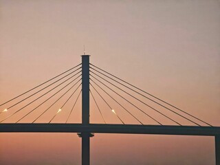 Obraz premium Silhouette of a cable-stayed bridge against a warm sunset sky, showcasing architectural elegance