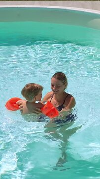 Smiling mother and her son wearing orange floaties, enjoying playtime in a swimming pool together
