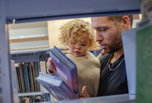 Adult male and young child browsing books together in a library. Cleveland, Ohio, USA
