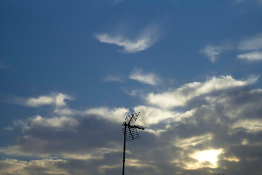 A silhouette of an antenna against a dramatic sky at dusk with sunrays piercing through clouds