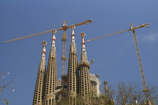 Sagrada Familia basilica under construction with cranes against a clear blue sky in Barcelona, Spain