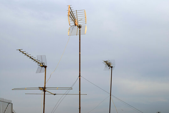 Three different sized rooftop television antennas against a pale sky at dusk