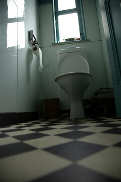 Low angle view of a clean bathroom with a white toilet, checkered floor, and a small window allowing natural light to come through, Auckland, New Zealand