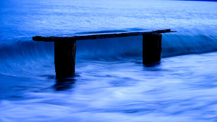 Wooden pier remains surrounded by gentle ocean waves, illuminated by a serene blue hue during twilight, creating a peaceful and tranquil seascape, Norwegian Point, WA, USA