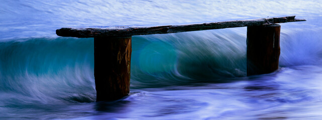 Wooden pier remnants stand against the swirling motion of blue ocean waves, creating a serene and dynamic coastal scene at dusk, Norwegian Point, WA, USA