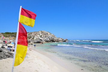 Red and yellow surf life saving flags, with out of focus turquoise colored sea and white sandy beach, Australia. Lifeguard, safety, drowning, death, statistics