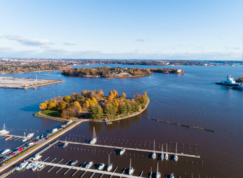 Aerial view of a marina with boats docked in neat rows, surrounded by autumn foliage and calm waters and Tervasaari island in Helsinki, with archipelago in the distance, Finland