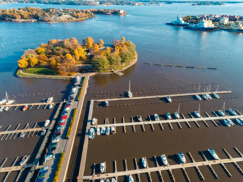 Aerial view of a marina with boats docked in neat rows, surrounded by autumn foliage and calm waters and Tervasaari island in Helsinki, with archipelago in the distance, Finland