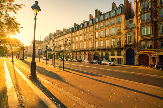 Parisian street at sunset with classic architecture, parked cars, and a street lamp, Paris, France