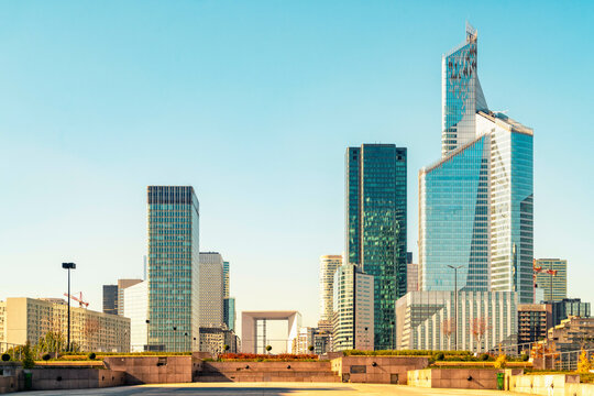 Modern skyscrapers dominate the skyline under a clear blue sky with a pedestrian walkway in the foreground in La Defense, Paris, France