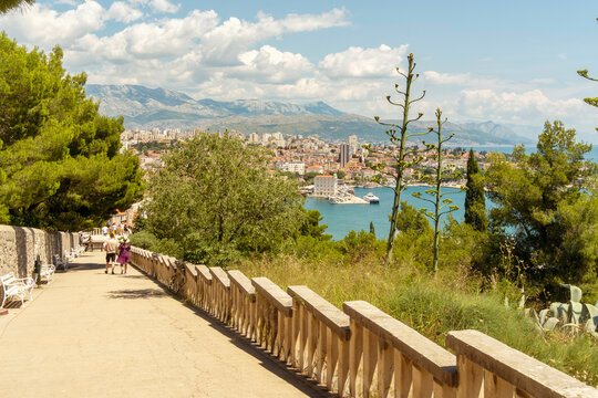 Coastal city of Split view from a hilltop path with a clear sky and a person walking along the railing, Croatia