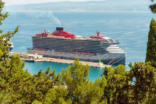 A large cruise ship sails on a blue sea viewed through green foliage under a clear sky, Split, Croatia