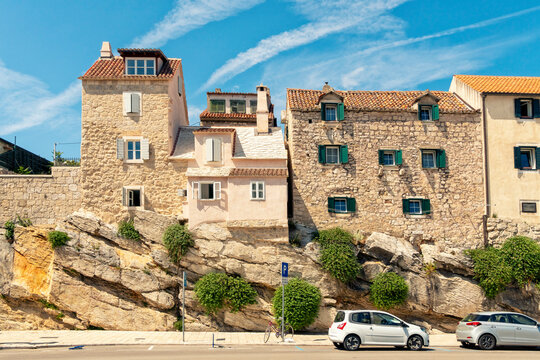 Traditional stone houses built upon a rocky outcrop beside a coastal road under a clear blue sky in Split, Croatia