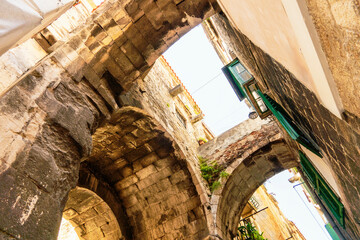 Sunlit stone alley with arches and green windows in an old city of Split, Croatia