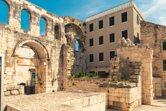 Ancient stone arches stand beside a modern building under a clear blue sky, blending historical architecture with contemporary construction by queen Helena's meadow, , Split, Croatia 