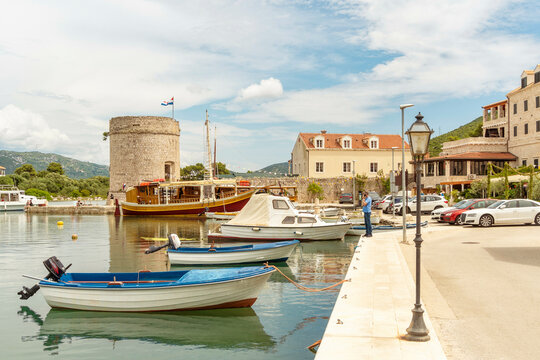 Boats moored by a stone quay in a picturesque coastal town with a round tower and clear blue sky, Mali Ston, Croatia