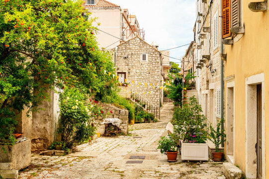 Cobblestone street in a quaint European village with stone buildings and greenery under a cloudy sky, Mali Ston, Croatia