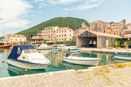 Boats moored in a calm marina with historical stone buildings and a green hill in the background under a clear sky, Mali Ston, Croatia